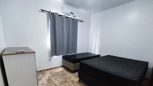 Ein kleiner, schlicht eingerichteter Raum mit einem Bett, einem Schrank und einem Fenster mit Vorhängen.