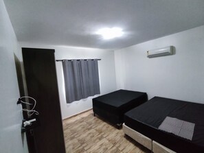 Pieni, yhden huoneen kokoinen majoituspaikka, jossa on puulattia, sänky, pieni pöytä, ikkuna verhoilla ja ovi.