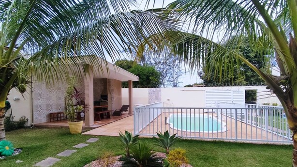 Ein Garten mit Swimmingpool, überdachter Terrasse und einer kleinen Gartenanlage.