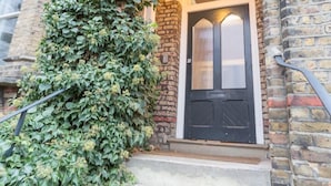 Een gebouwentree met een zwarte deur, stenen trappen en een hangende lamp.
