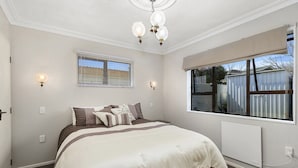 A bedroom with a large bed, a chandelier, a window with blinds, and a radiator.