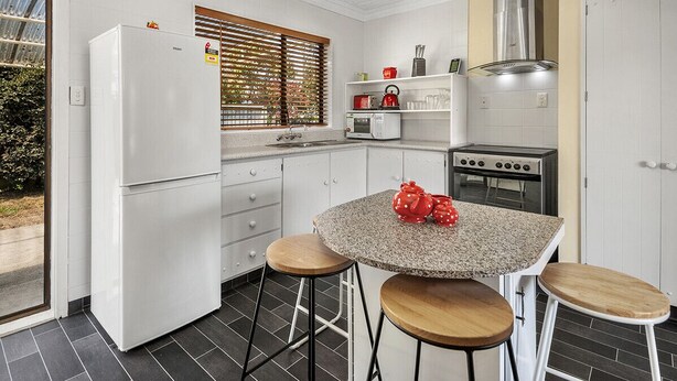 A compact kitchen with a refrigerator, stove, microwave, and a small dining area with stools.
