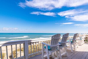 Een houten terras met witte Adirondack-stoelen, gericht op het strand.