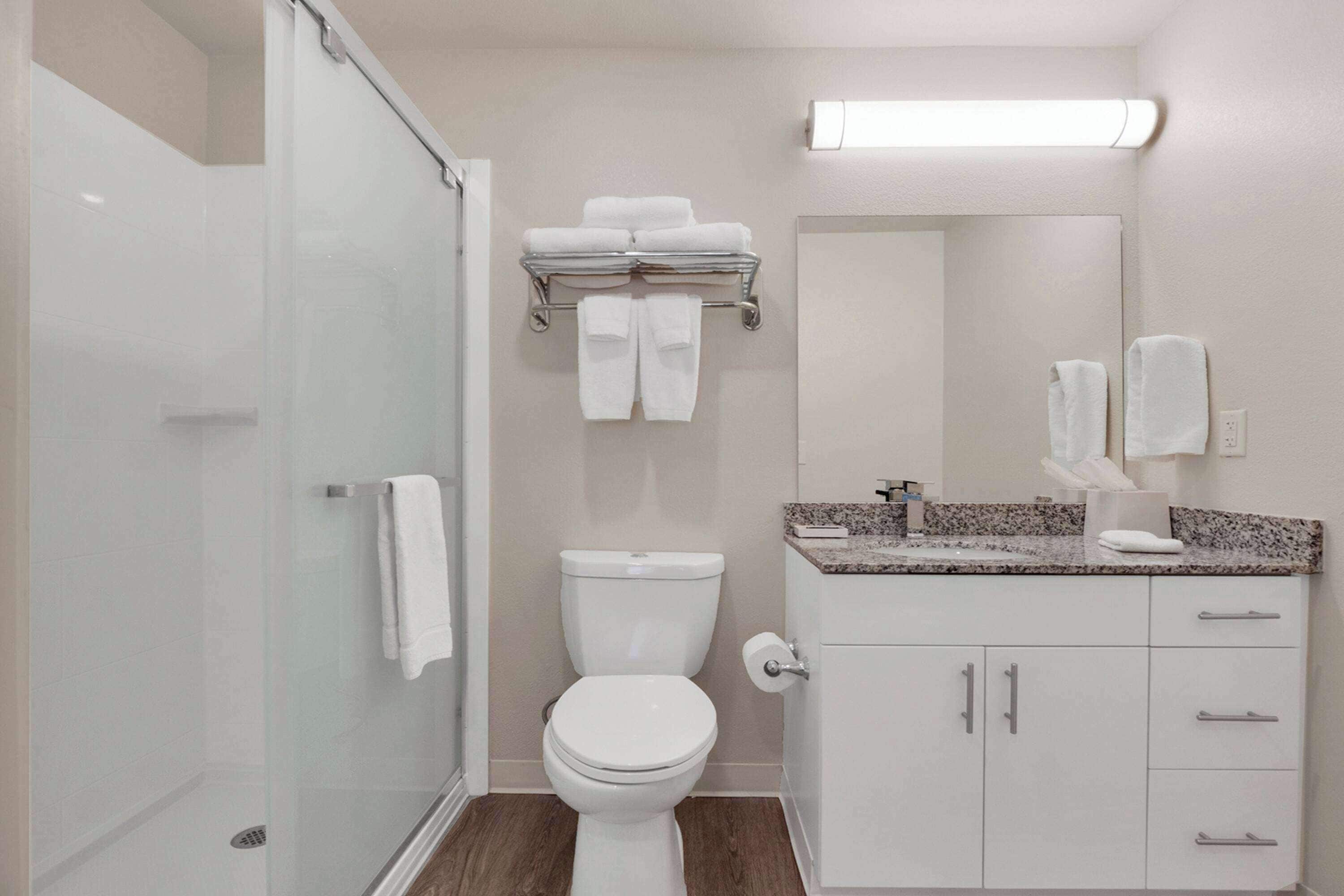 Une salle de bain moderne avec une douche à parois de verre, des toilettes blanches, un meuble-lavabo avec un plan de travail en granit et un miroir au-dessus du lavabo.