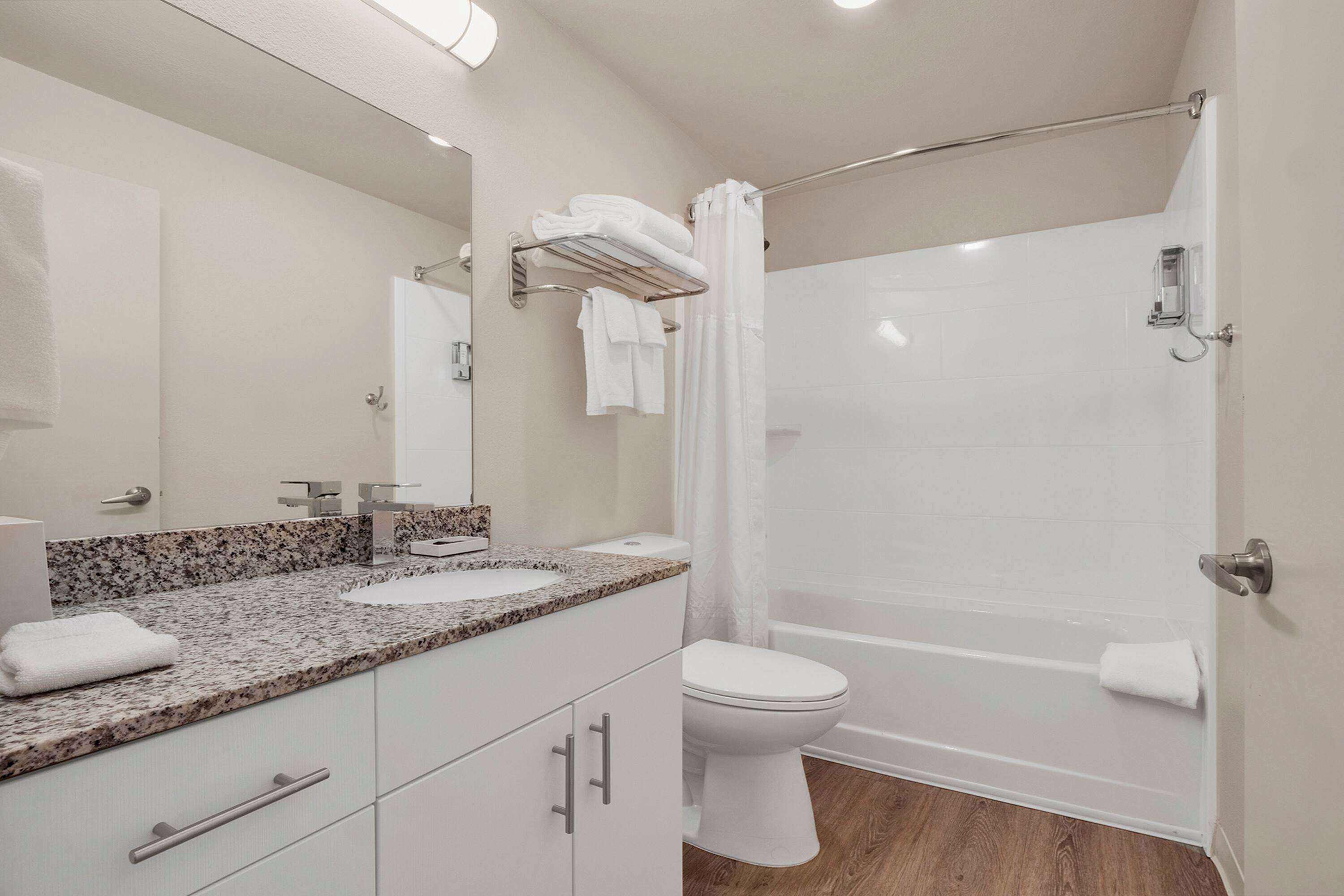 A modern bathroom with a granite countertop sink, a white toilet, and a glass shower enclosure.