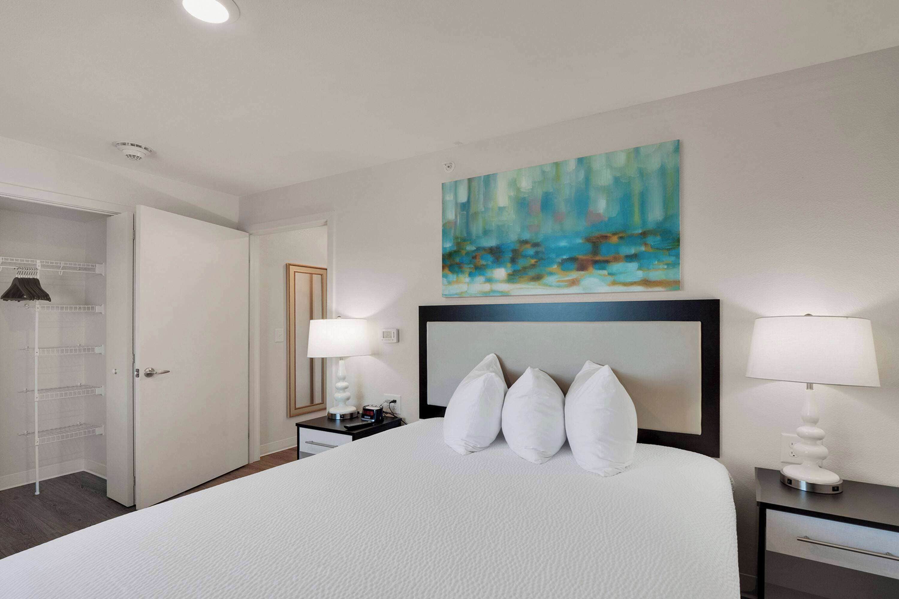 A hotel room with a large bed, two bedside tables with lamps, a wardrobe, and a painting on the wall.