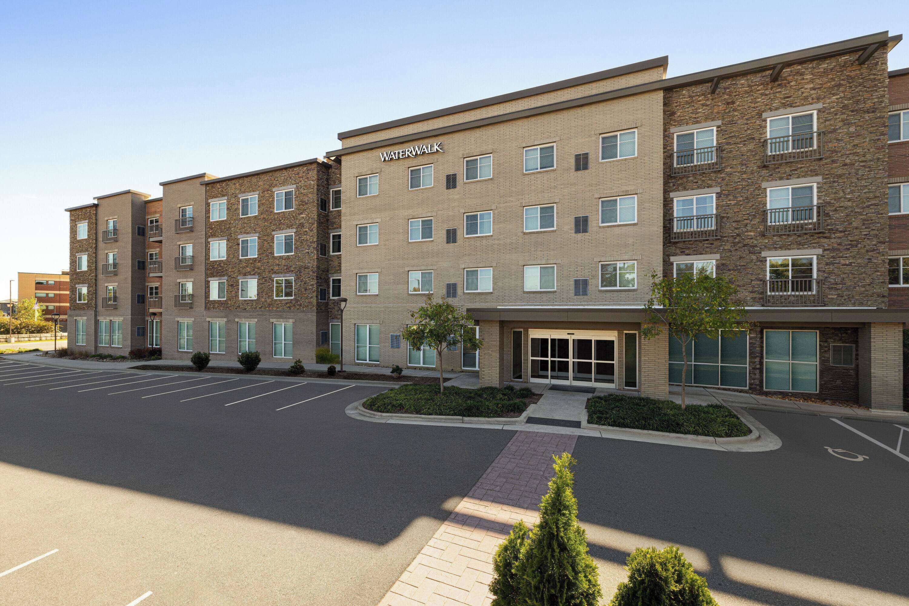 A multi-story building with a "Waterwalk" sign, featuring a brick facade, multiple windows, and a parking lot in front.