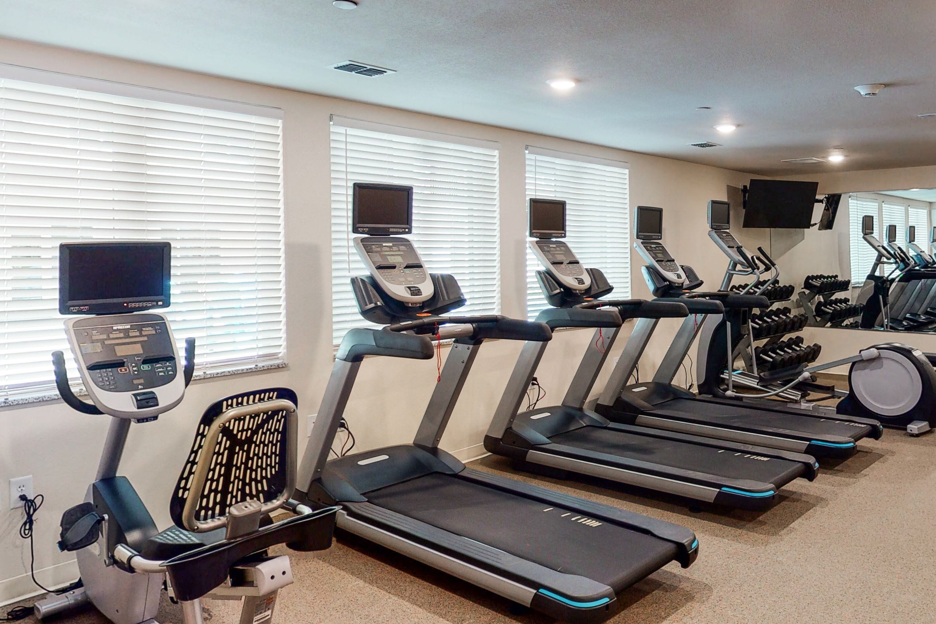 Un gimnasio con cintas de correr, bicicletas estáticas y una banca para pesas.