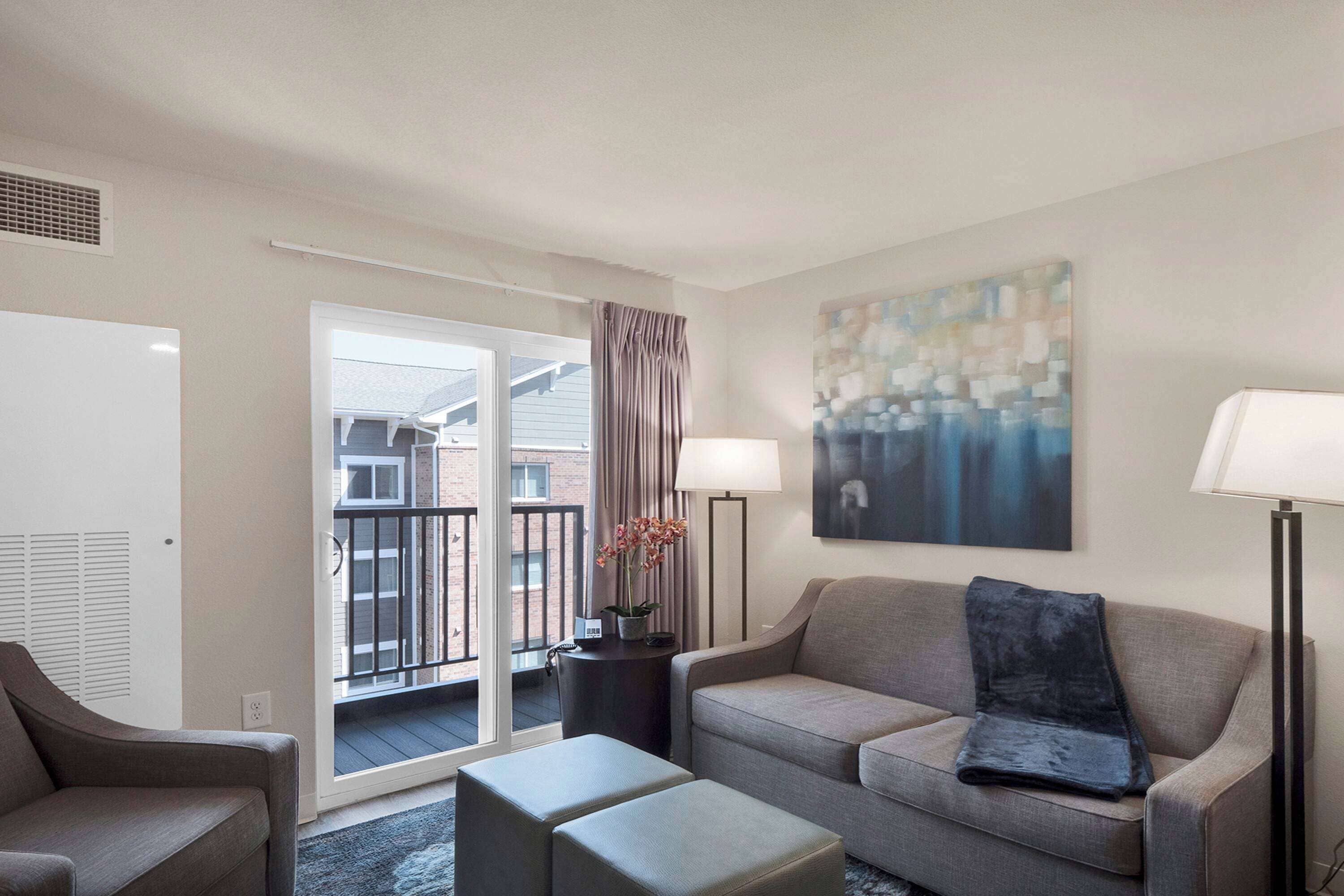 A modern living room with a grey sofa, two matching ottomans, a floor lamp, and a painting on the wall.