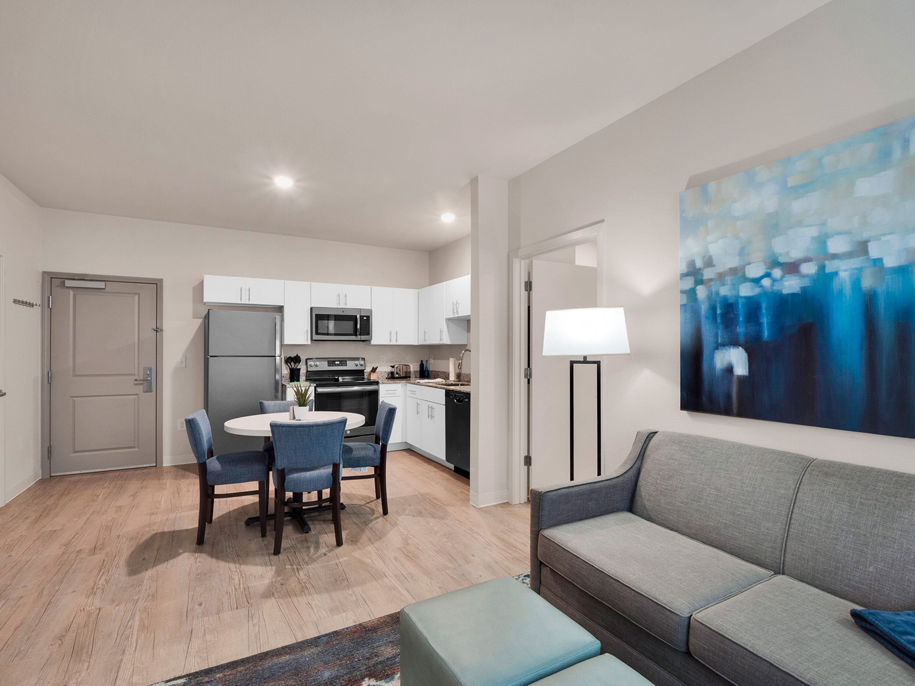 A modern apartment with a dining area, kitchenette, and a living room with a sofa and a painting.