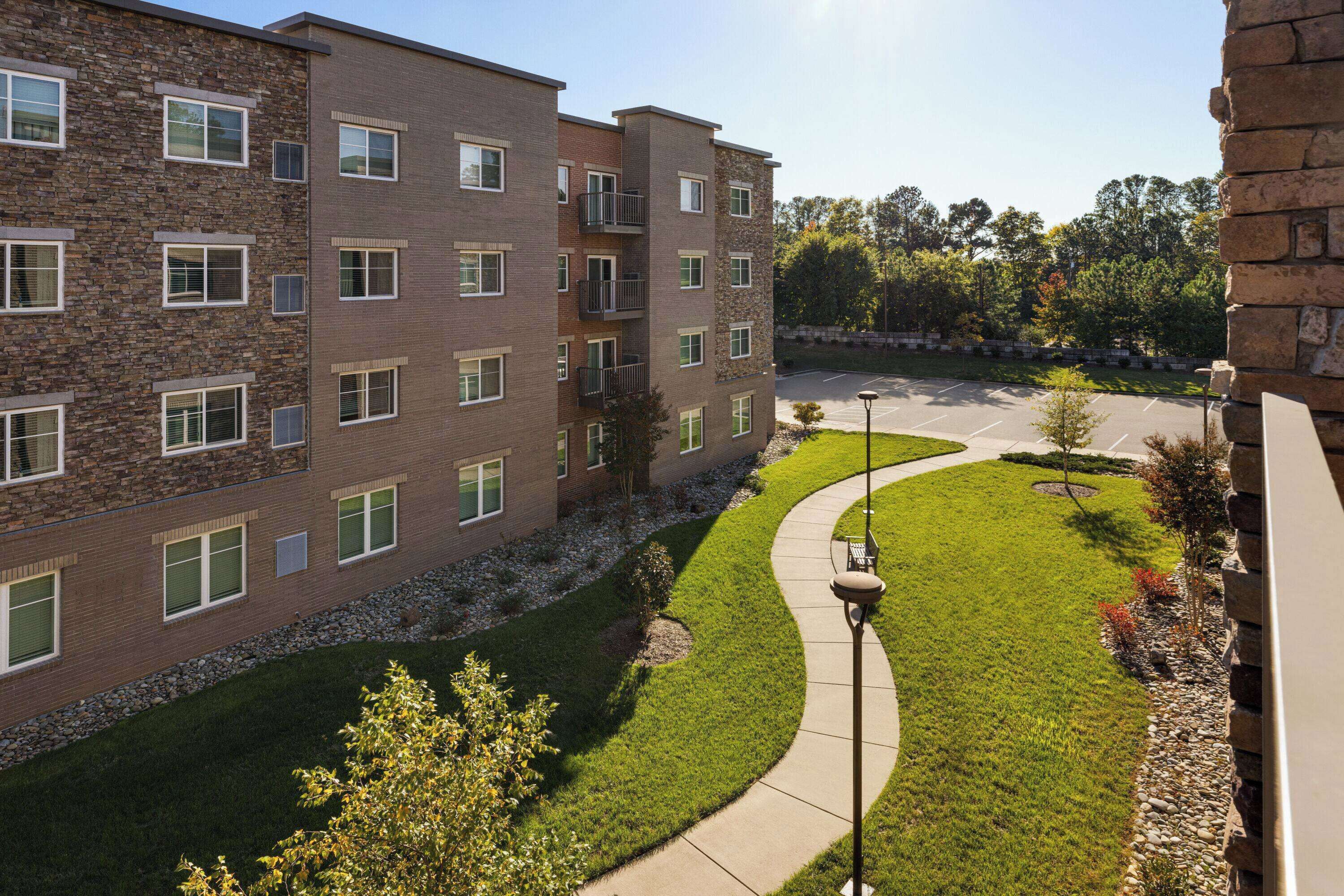 A multi-story building with a stone facade, a parking lot, and a well-maintained lawn.