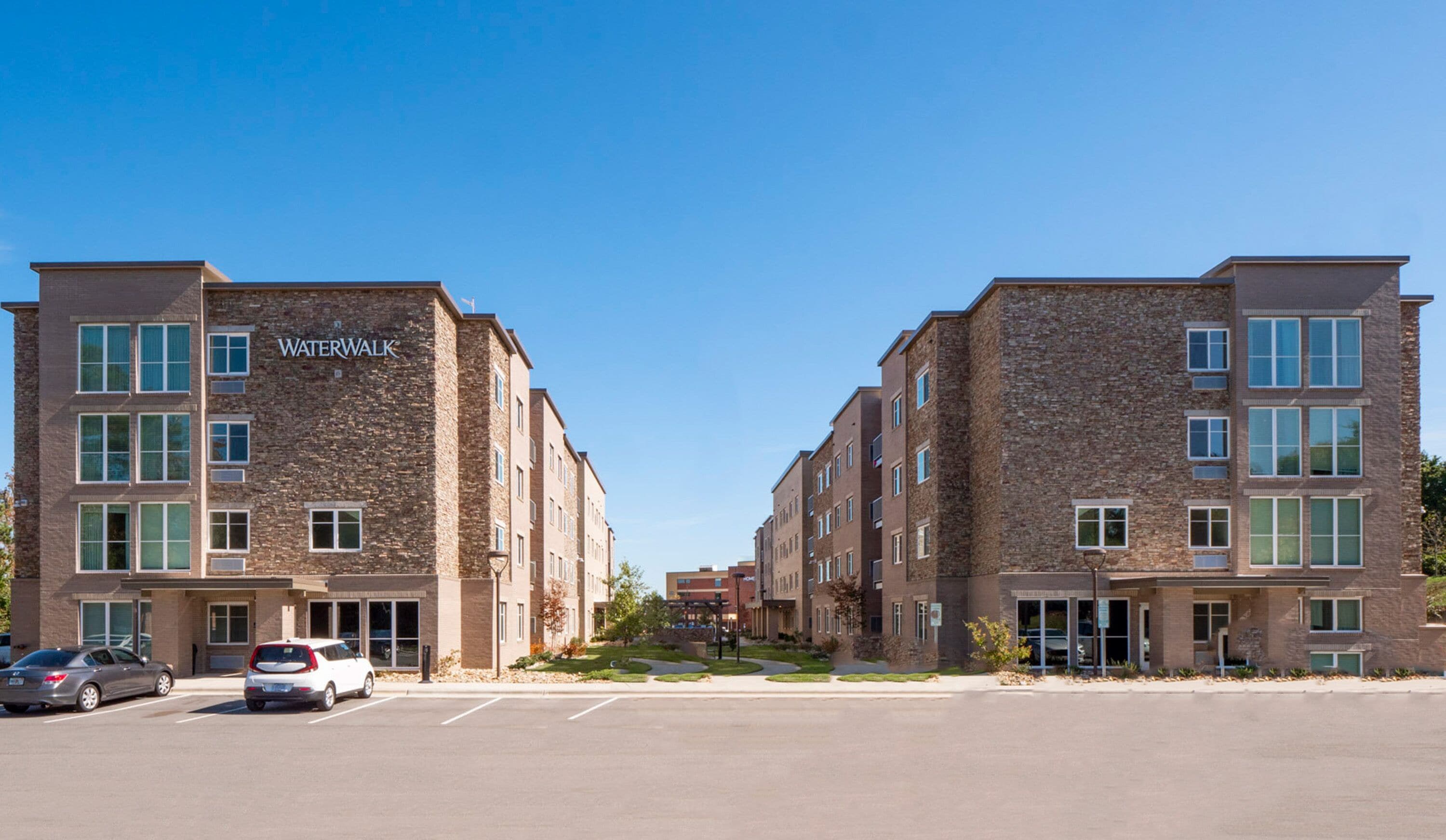 A modern building with the name "WaterWalk" on the facade, featuring a symmetrical design with multiple windows and a parking lot in front.