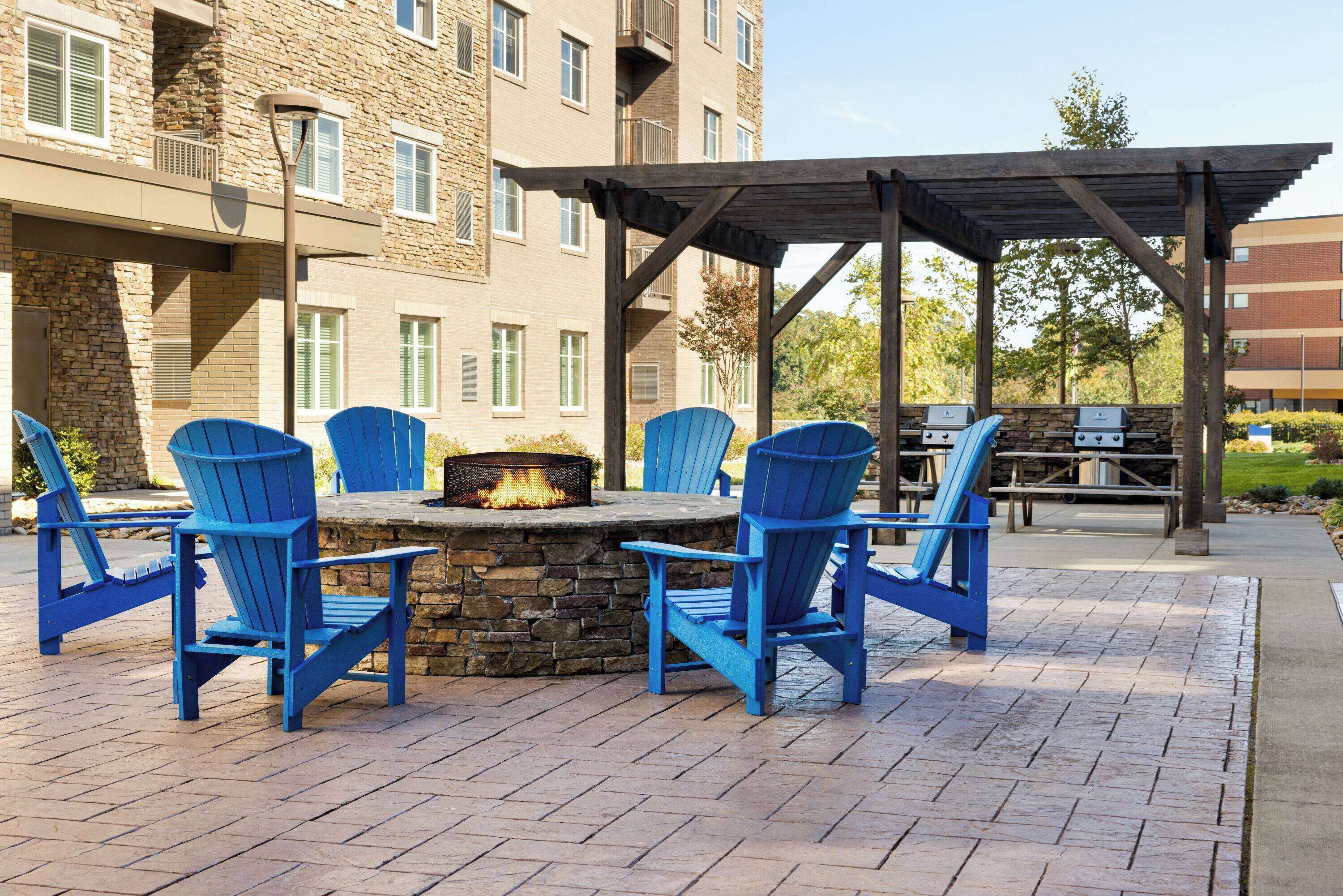 Un patio al aire libre con un pozo de fuego de piedra, sillas Adirondack azules y una pérgola.