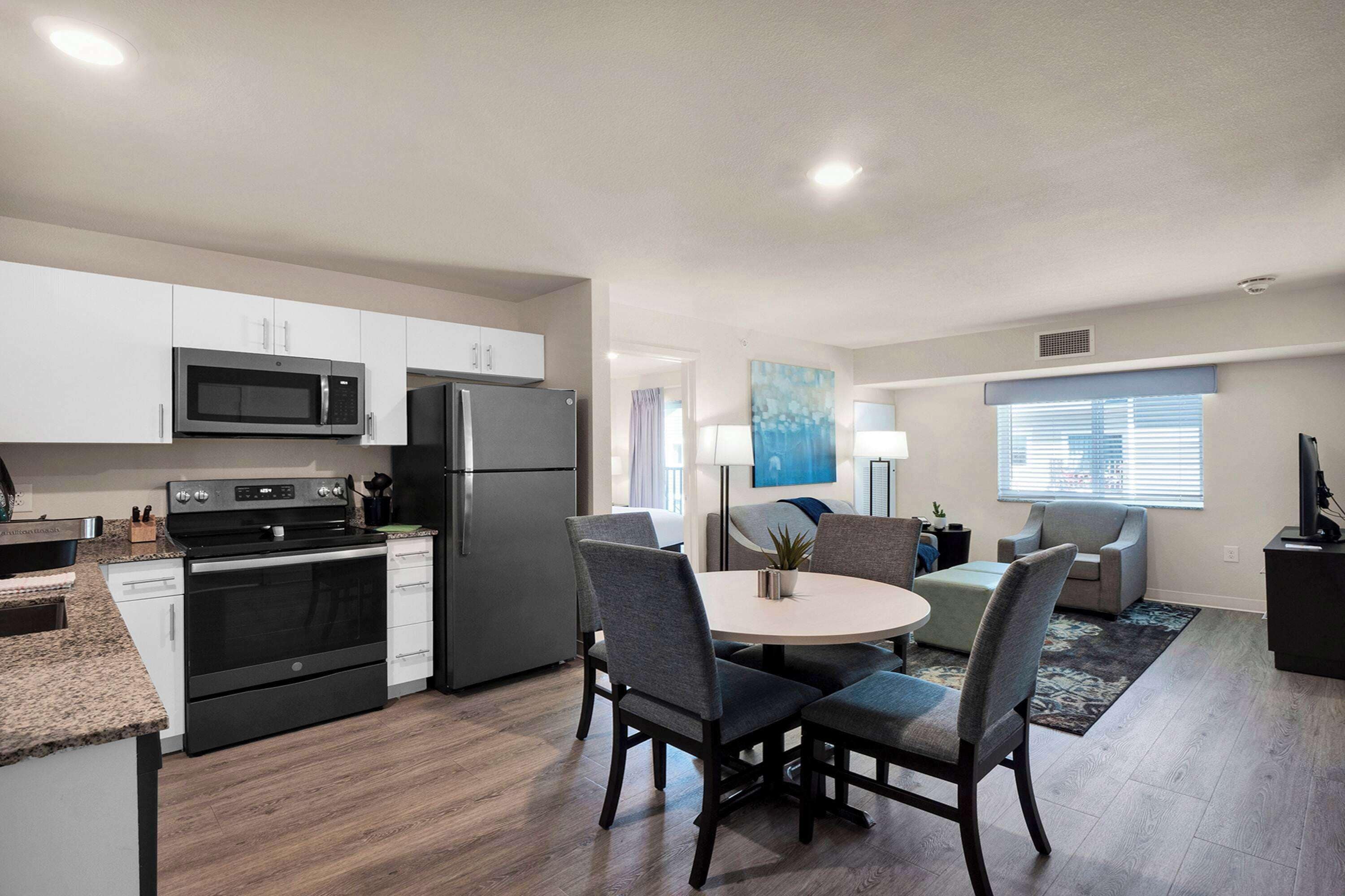 A modern kitchen with a microwave, stove, and refrigerator. There is a dining area with a round table and chairs.