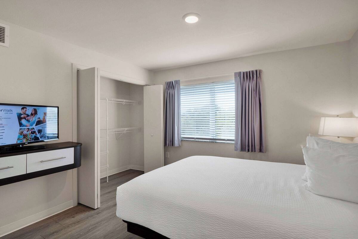 Ein Hotelzimmer mit Bett, Fernseher, Kleiderschrank und einem Fenster mit Vorhängen.
