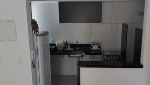 Une cuisine compacte avec des meubles blancs, un plan de travail noir, une cuisinière encastrée et un petit évier.