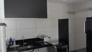 Une cuisine moderne avec des carreaux blancs, un plan de travail noir, un évier en acier inoxydable, une cuisinière et un réfrigérateur noir.