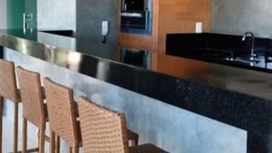 Une cuisine moderne avec un plan de travail noir, des suspensions bleues et des tabourets de bar en osier.