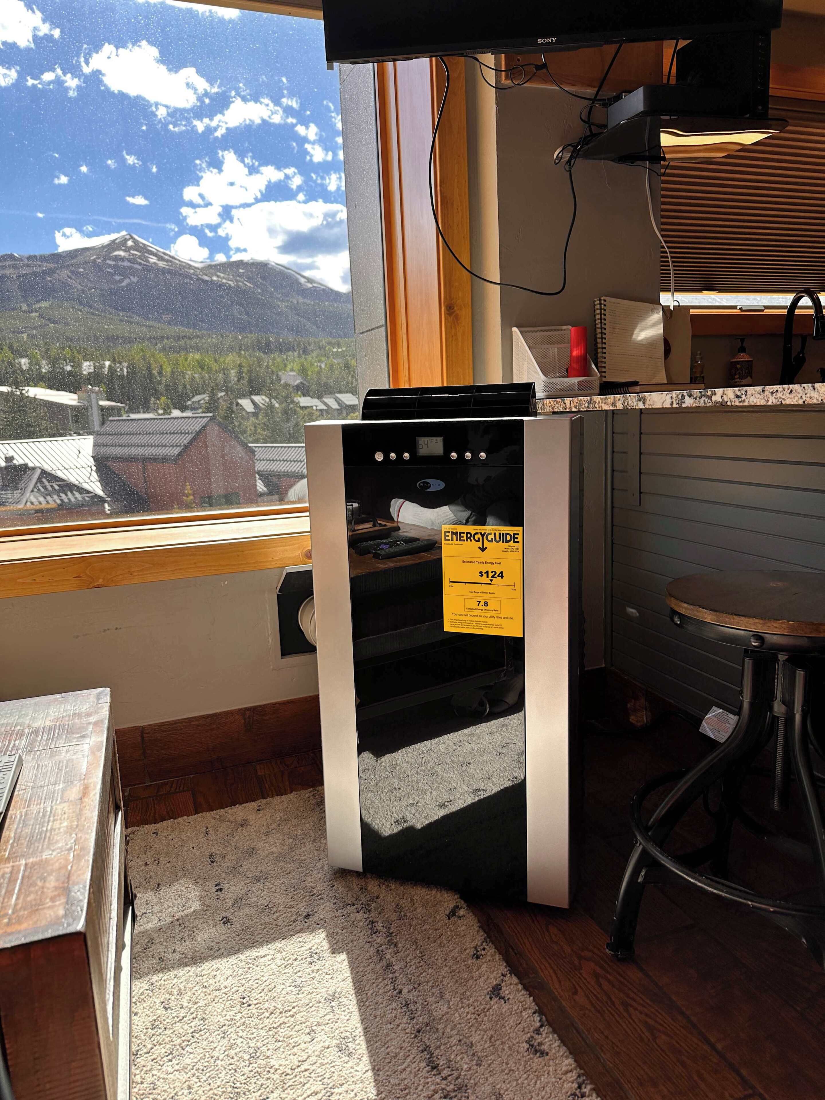 A kitchen with a view of mountains, a refrigerator, a sink, and a window.