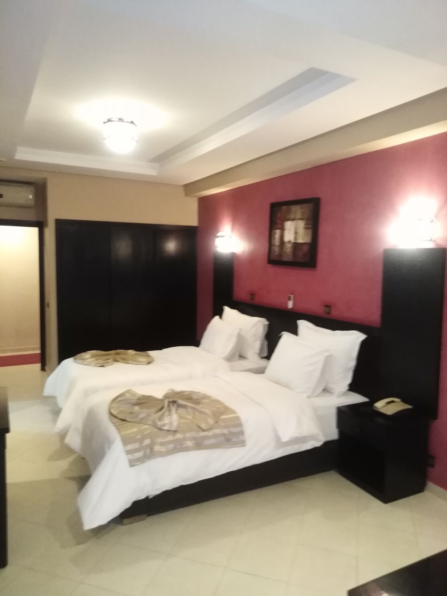 A hotel room with a bed, bedside tables, and a wall-mounted light fixture.