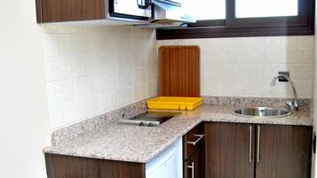 Una cocina compacta con gabinetes de madera oscura, encimera de granito, microondas integrado y un lavamanos.