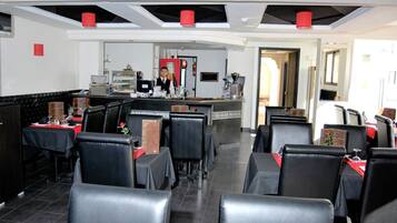 Un restaurante con sillas de cuero negro, mesas con manteles rojos, una barra con una persona detrás y un diseño de techo moderno.