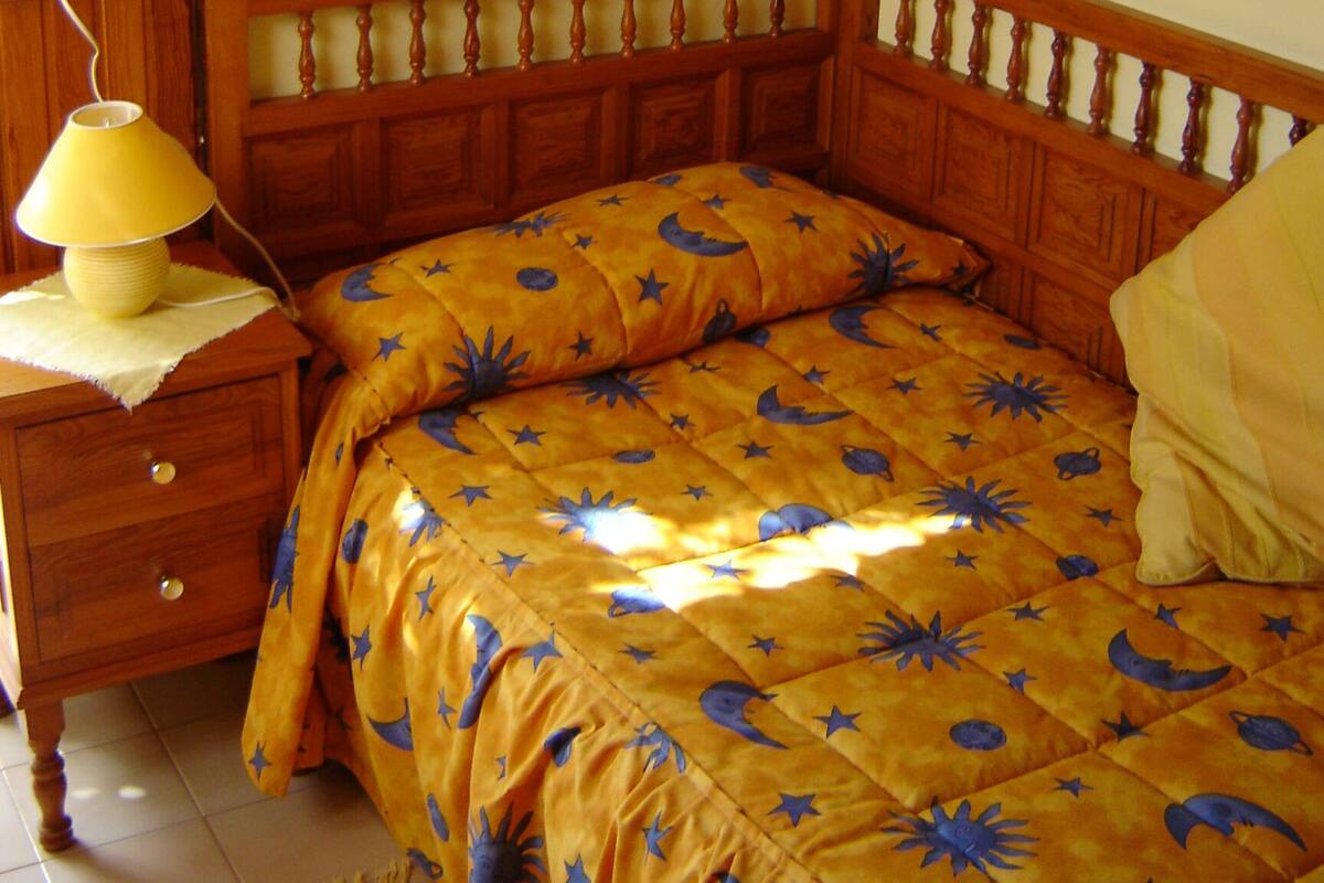 A bedroom with a wooden bed, a nightstand with a lamp, and a shelf with decorative items.