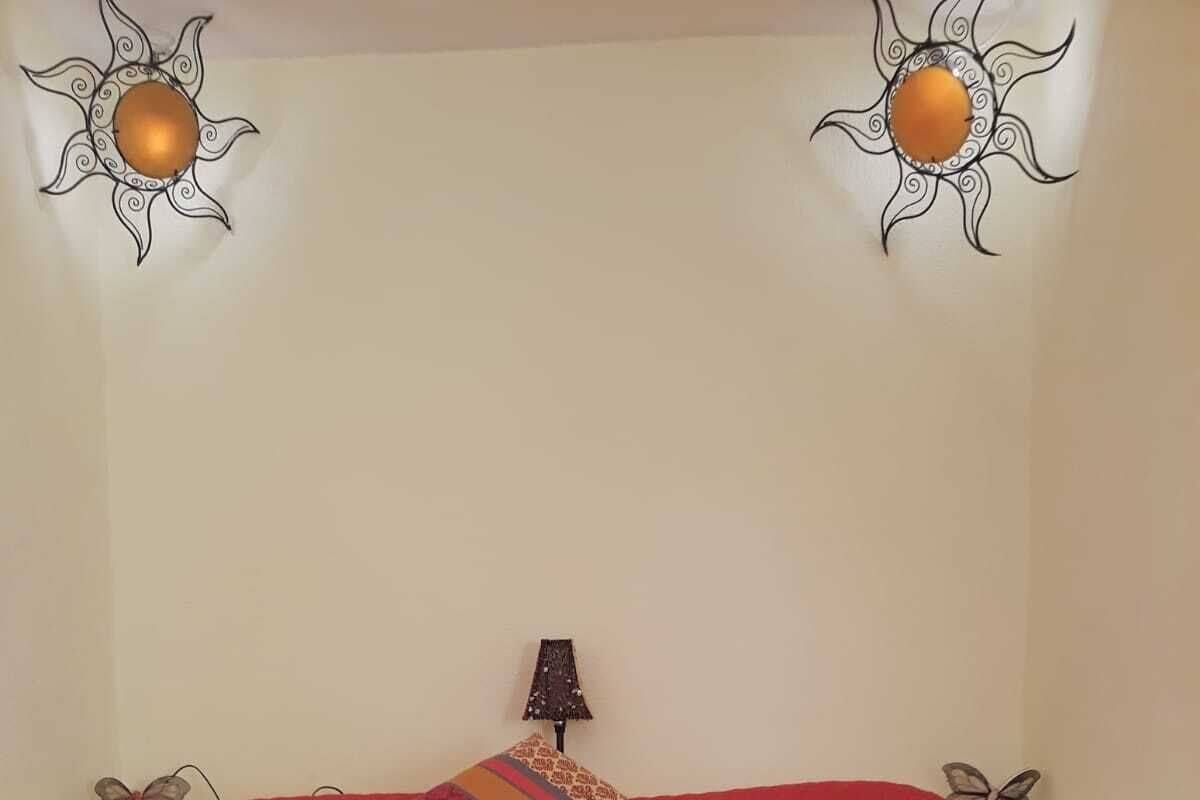 A bedroom with a red bedspread, a decorative pillow, a lamp, and wall art.