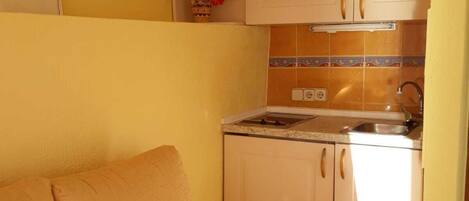 Un espacio habitable compacto con sofá, una pequeña zona de cocina y un solo armario.