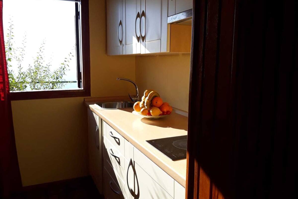 A small kitchen with a window, a sink, and a plate of fruit.