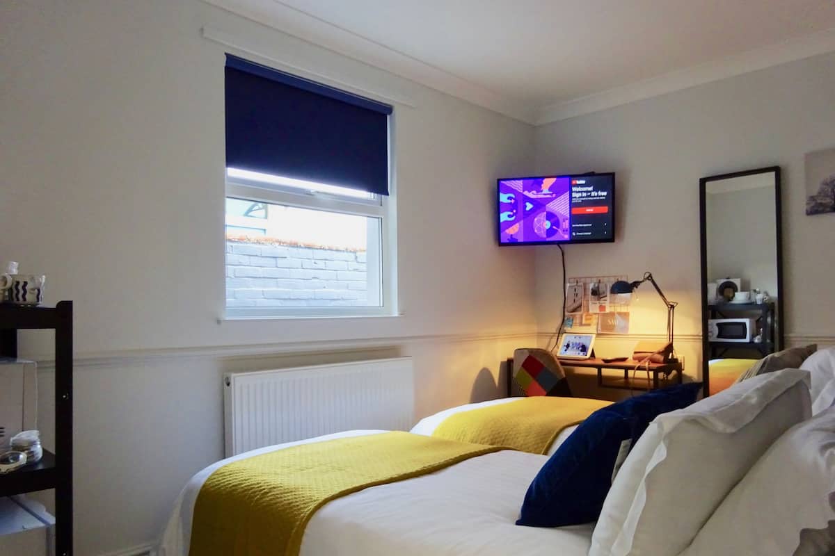 A hotel room with a bed, a desk with a computer, a television, and a window with blinds.