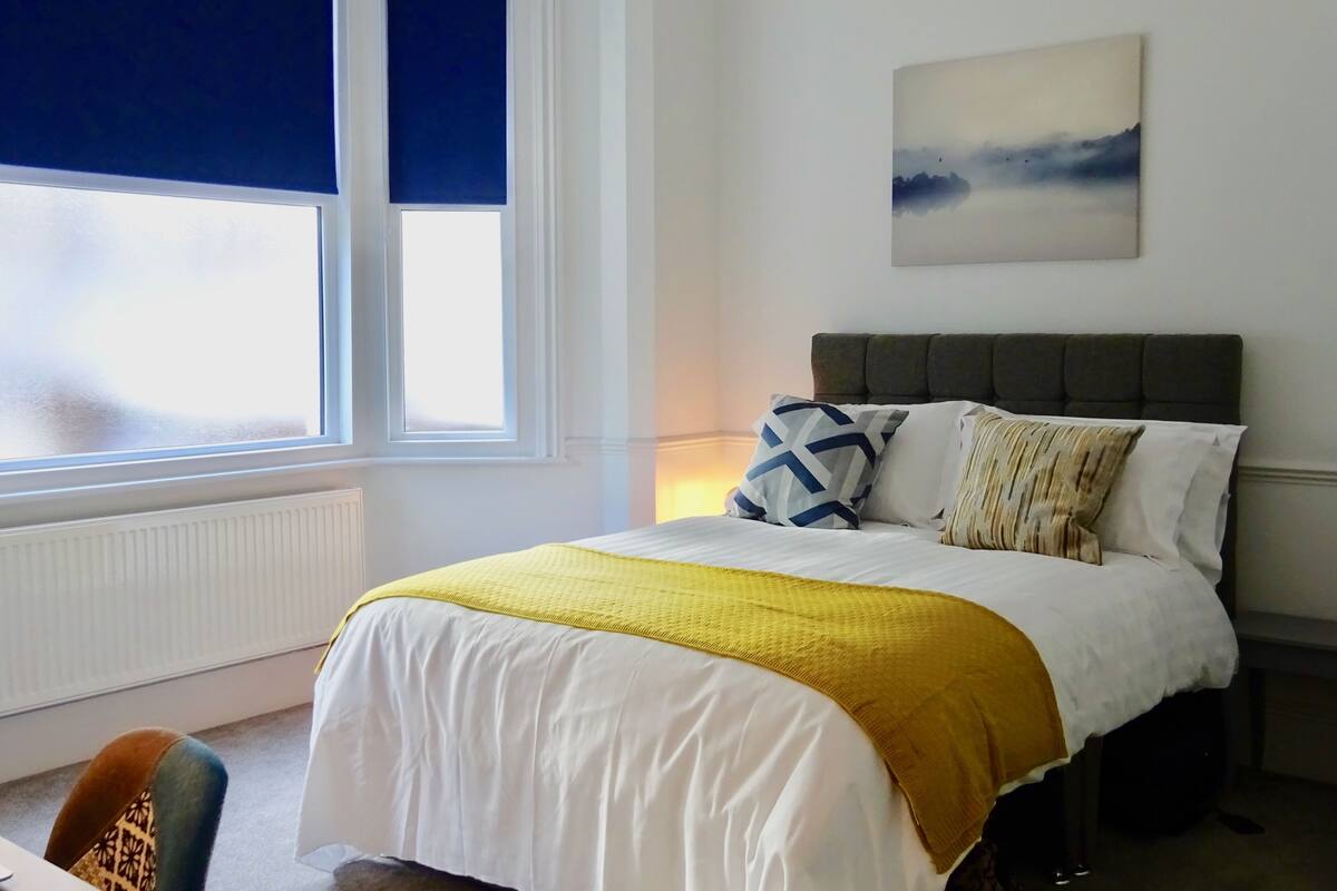 A bedroom with a bed, a window, a painting, and a chair.