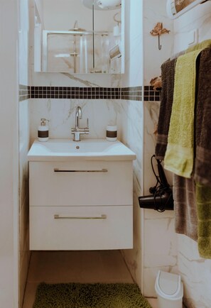 Une salle de bain avec un lavabo blanc, un miroir, un porte-serviettes avec une serviette et une petite poubelle.