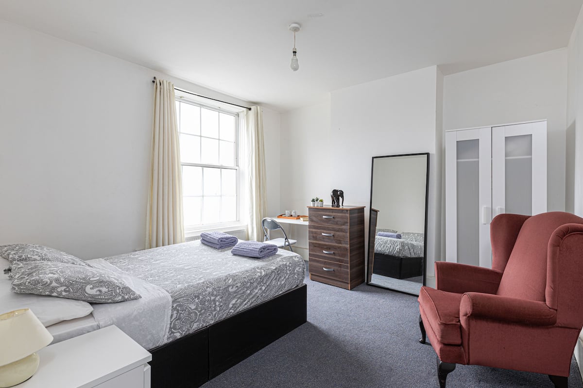 Une chambre à coucher avec un lit, une commode, une chaise et un miroir.