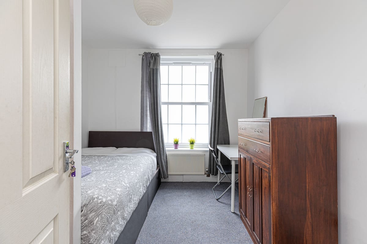Une chambre à coucher avec un lit, un bureau, une commode et une fenêtre avec des rideaux.