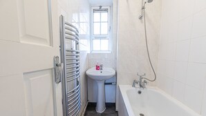 Un baño con una bañera blanca, un lavamanos pedestal y un ventanal sobre el lavamanos.