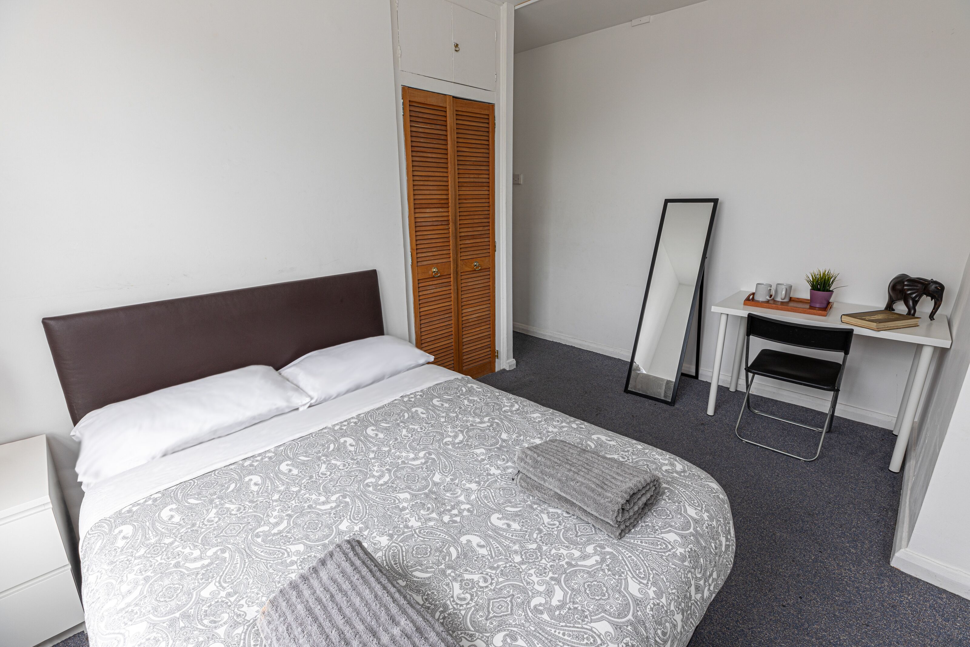 Une chambre à coucher comprenant un lit, une armoire, un bureau avec un miroir et une petite étagère avec quelques objets.