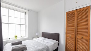 Un dormitorio con cama, ventana, mesita de noche, lámpara y armario.