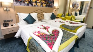 A hotel room with two beds, each with a heart-shaped floral arrangement on the bedspread. There is a large mirror on one wall, a nightstand with a lamp, and a painting above the bed. - Lahdat Hotel Al Balad (Jeddah)