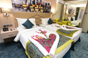 A hotel room with two beds, each with a heart-shaped floral arrangement on the bedspread. There is a large mirror on one wall, a nightstand with a lamp, and a painting above the bed. - Lahdat Hotel Al Balad (Jeddah)