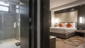 Una habitación de hotel moderna con una cama grande, una mesita de noche y una zona de ducha con paredes de vidrio.