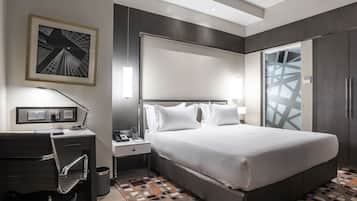 Een moderne hotelkamer met een groot bed, een bureau met stoel, een nachtkastje en een lijst met afbeelding aan de muur.