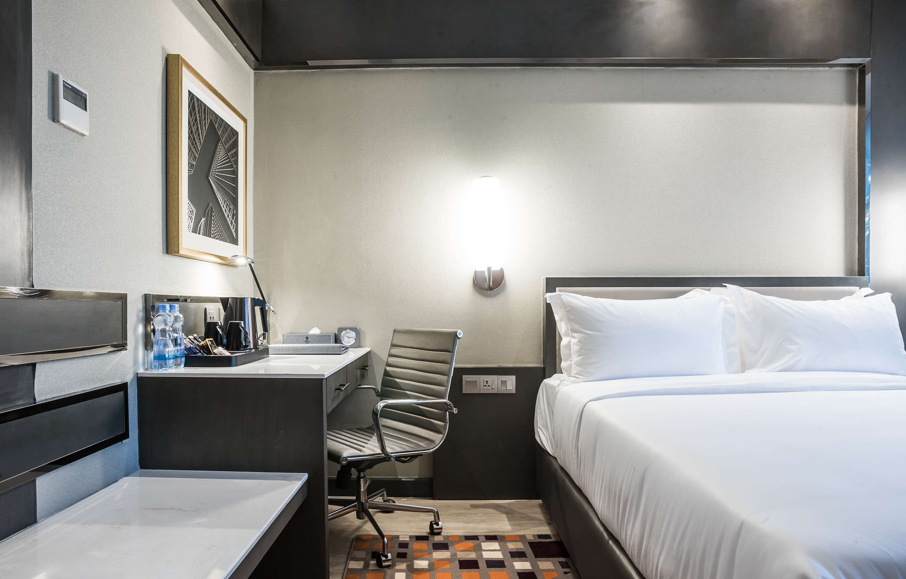 A hotel room with a bed, desk, chair, and a framed picture on the wall.