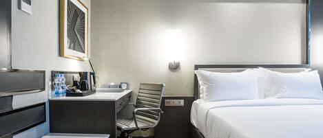A hotel room with a bed, desk, chair, and a framed picture on the wall.