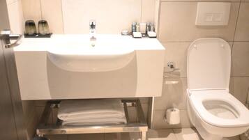 A bathroom with a white sink, toilet, and a shelf with towels and toiletries.