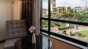 A hotel room with a large window, a sofa, a table, and a vase with a flower. - Best Western Premier Westlands (Nairobi)
