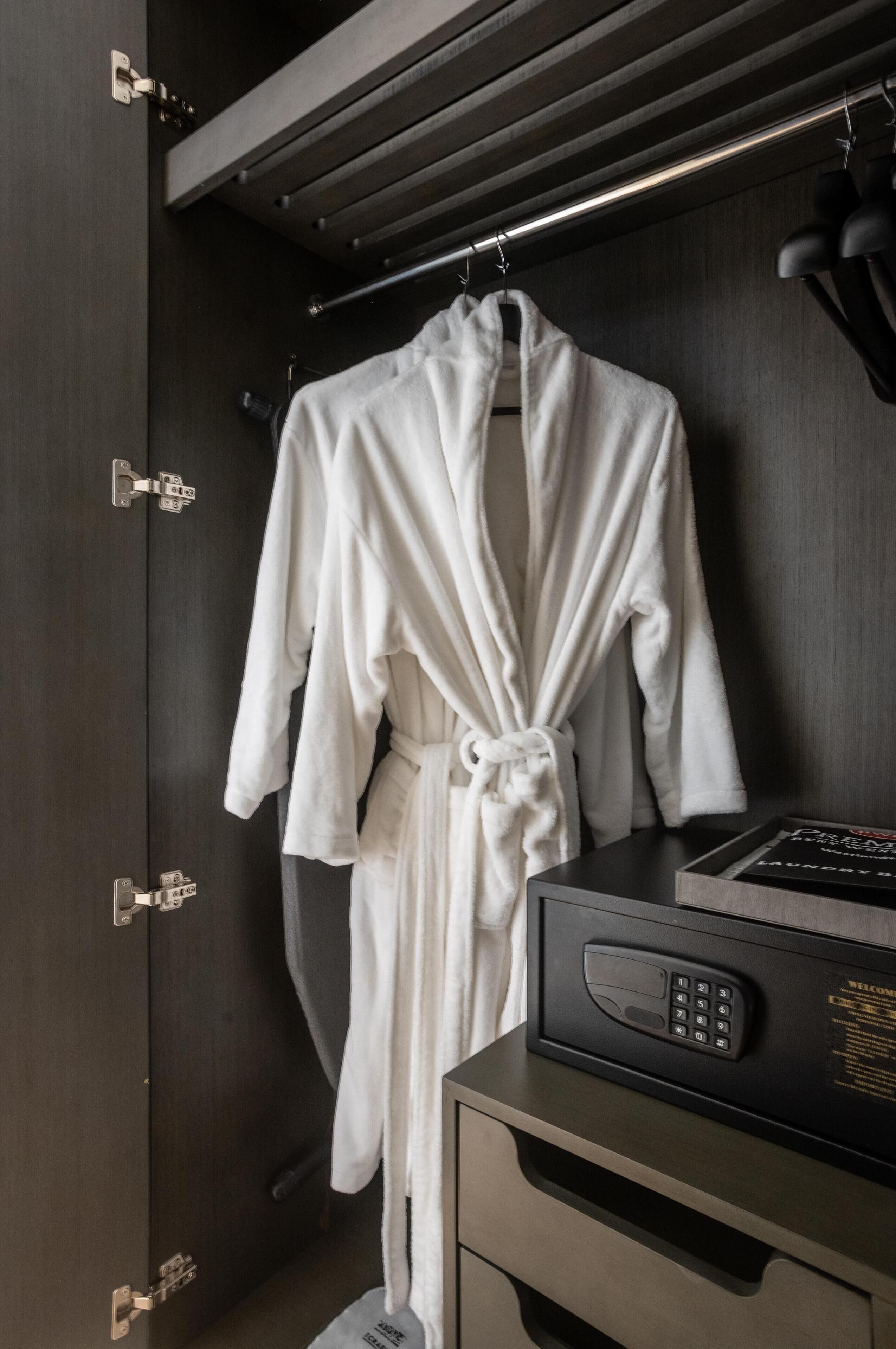 A hotel room with a dark wooden wardrobe, a white robe hanging on the door, and a black electronic device on the dresser.