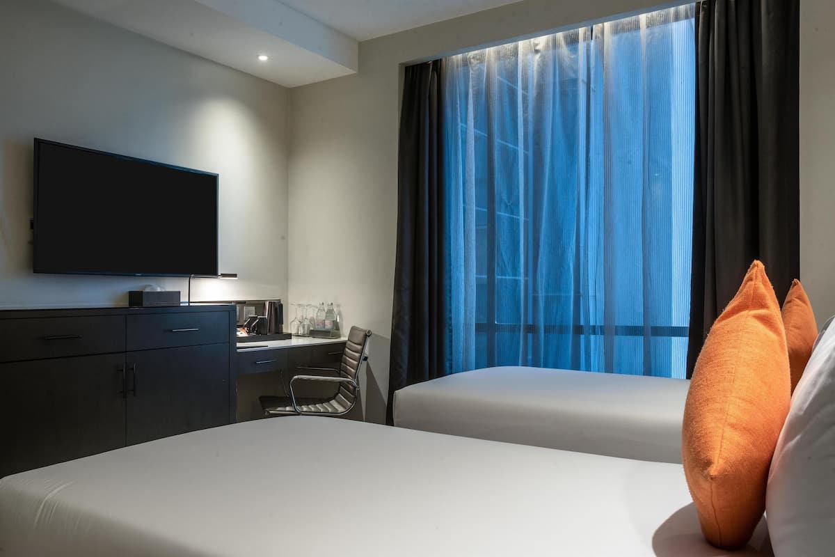 Una habitación de hotel con cama, escritorio, silla, televisor y ventana con cortinas.