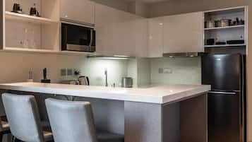Una cocina moderna con una isla central, taburetes de bar, un microondas empotrado y un refrigerador negro.