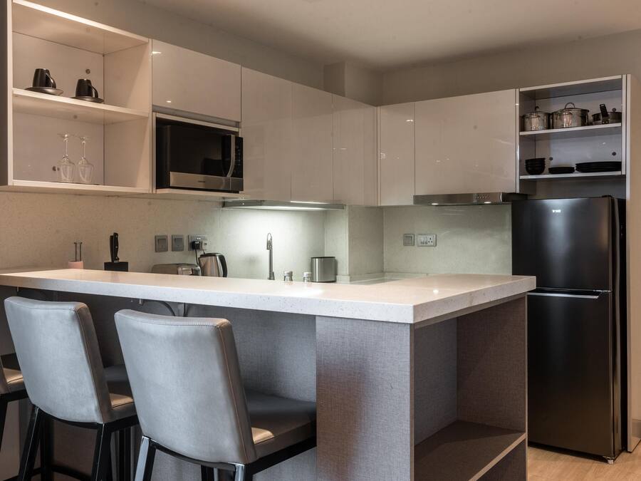 Una cocina moderna con una isla central, taburetes de bar, un microondas empotrado y un refrigerador negro.